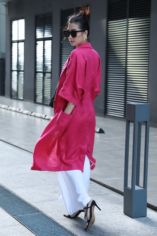 Woman in a fuchsia pink coat and white pants walking on a sidewalk