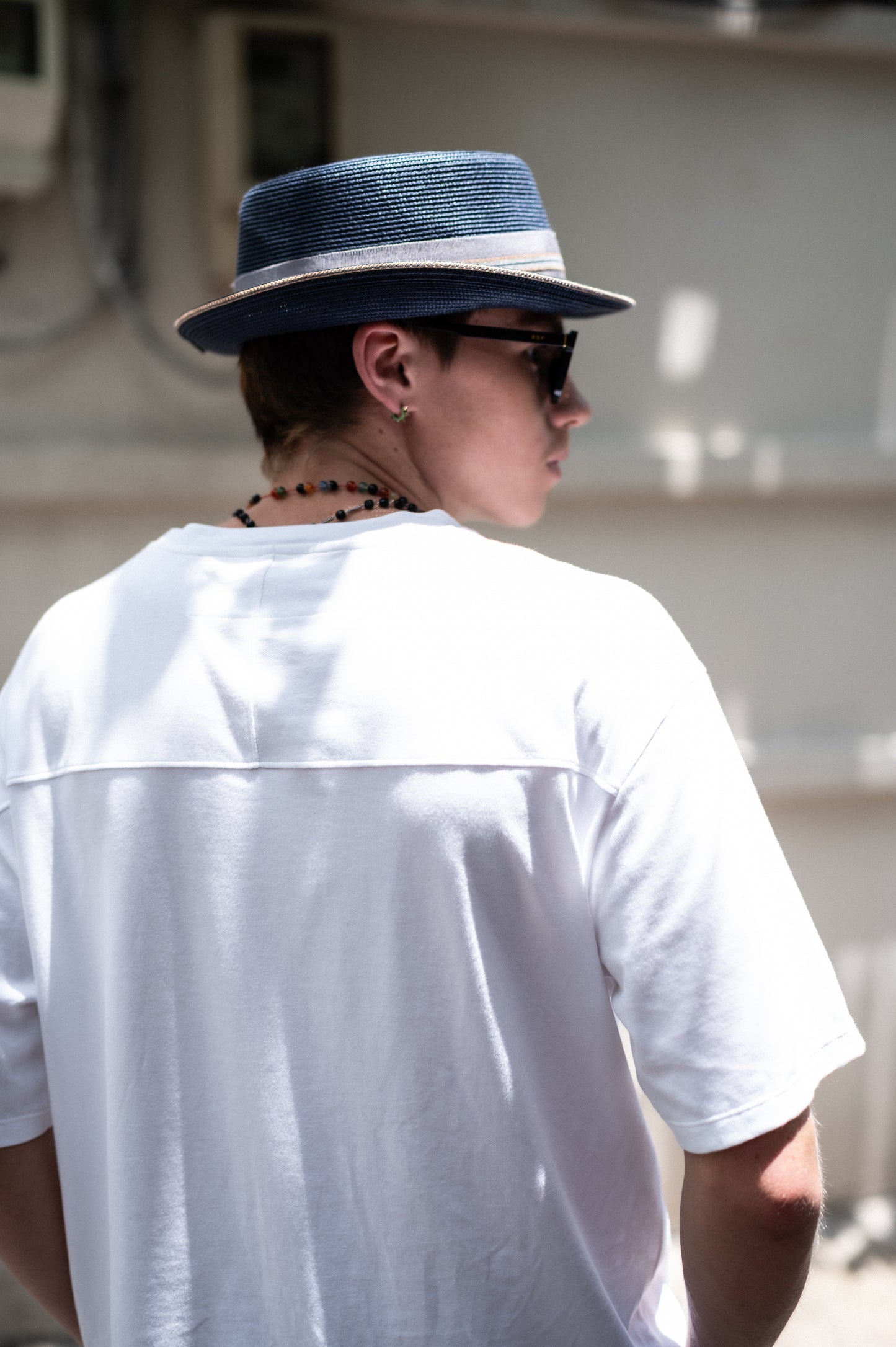 Person wearing a blue hat and sunglasses, white t-shirt showing back yolk detail. facing away from the camera.