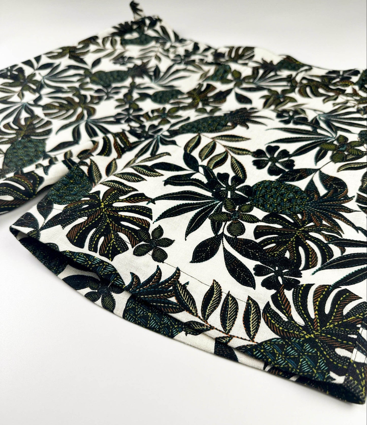 Edge detail - Black tropical floral patterned linen shorts on a natural white background