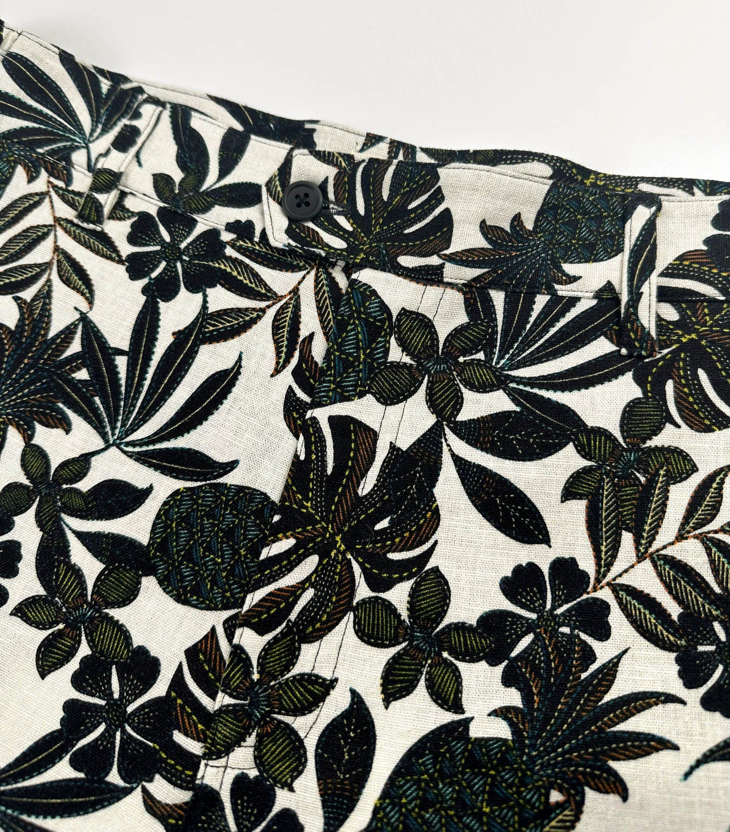 Close up of front zipper of black tropical floral patterned linen shorts on a natural white background