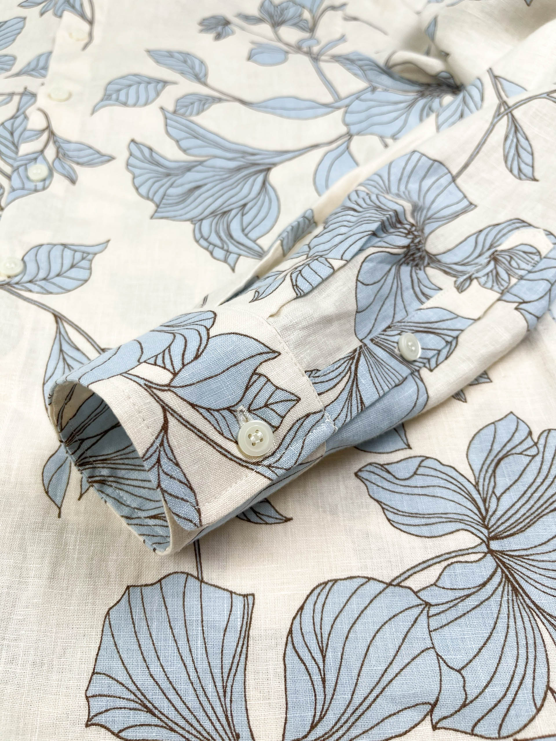 Blue Hibiscus linen long sleeve button-up shirt lay flat cuff detail view, light blue hibiscus print on natural white linen