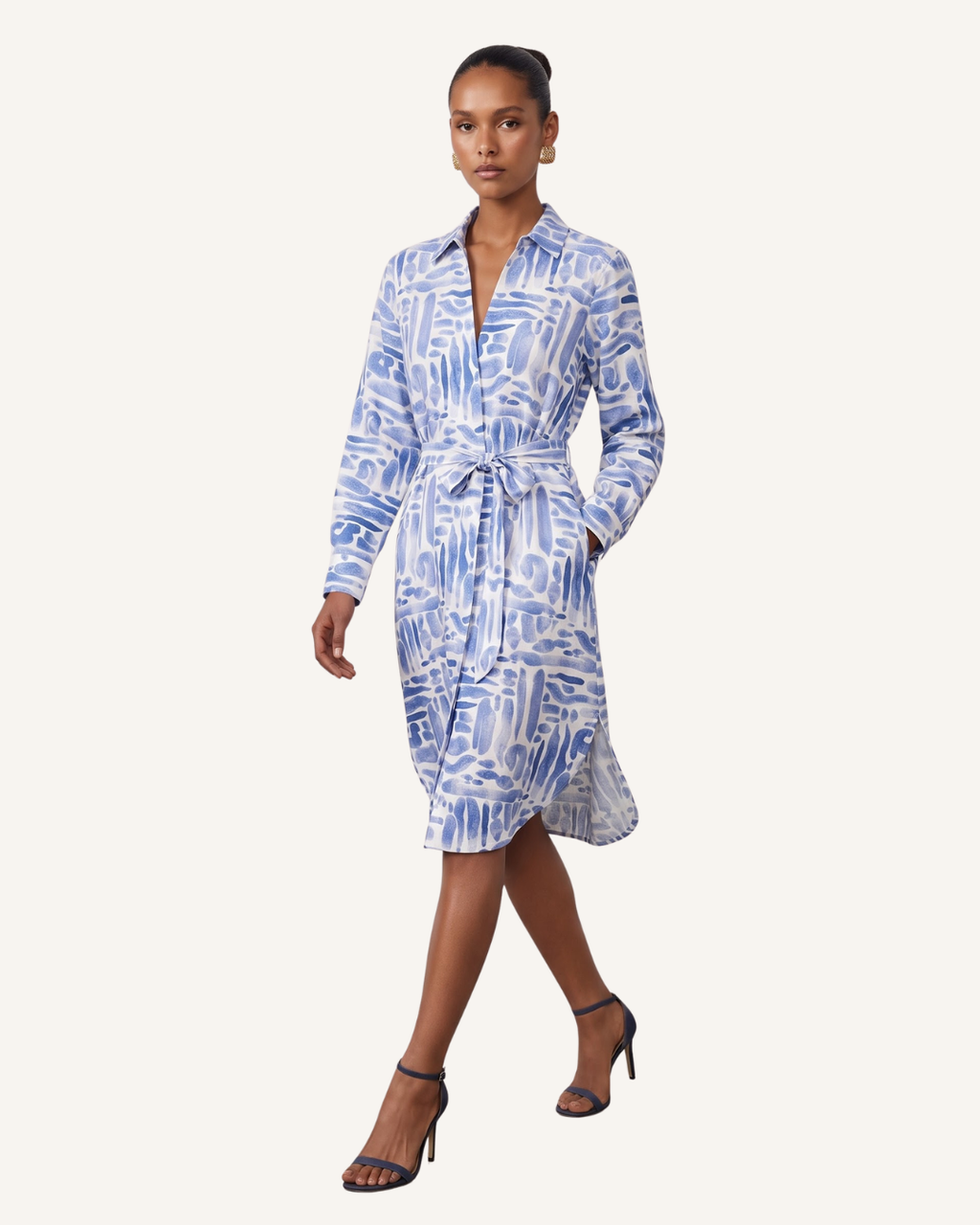 A model wearing a blue and white abstract patterned long-sleeve wrap dress with a tie waist, paired with black high-heeled sandals, against a solid off-white background.
