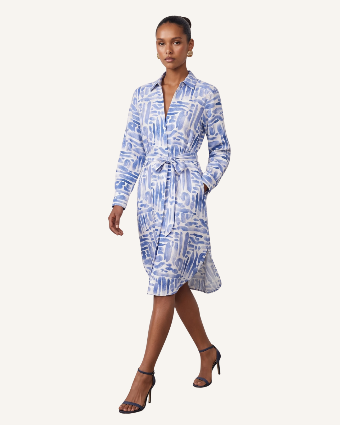 A model wearing a blue and white abstract patterned long-sleeve wrap dress with a tie waist, paired with black high-heeled sandals, against a solid off-white background.
