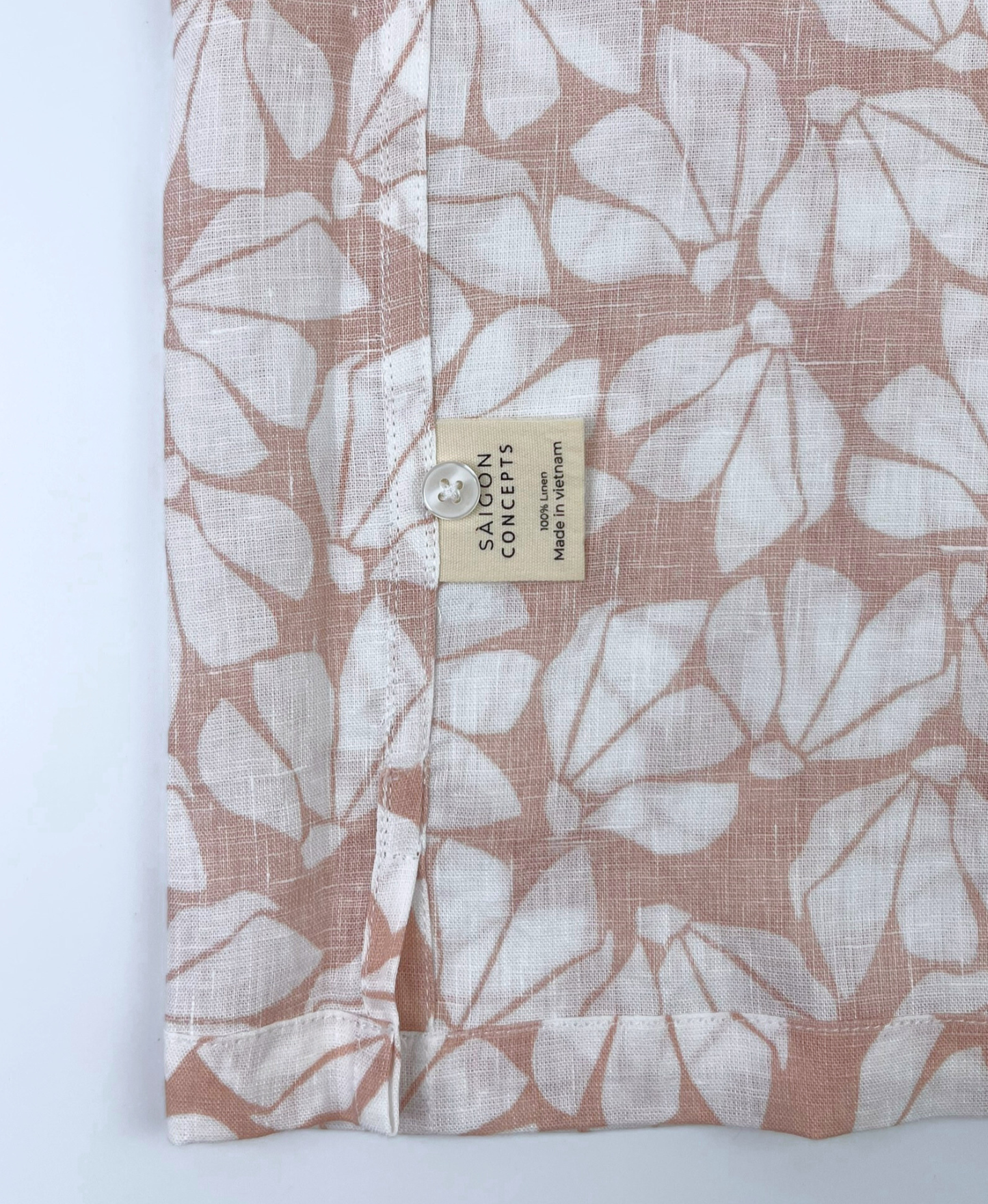 Close-up of white floral print on pink linen fabric, breathable natural fibre Hawaii shirt - care label and spare button detail