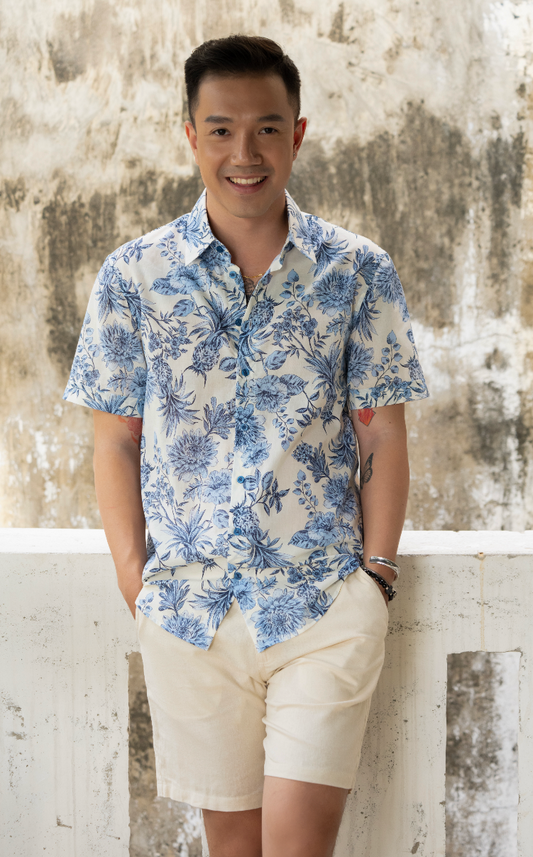 Man wearing a blue and white floral shirt and white shorts against a textured wall.