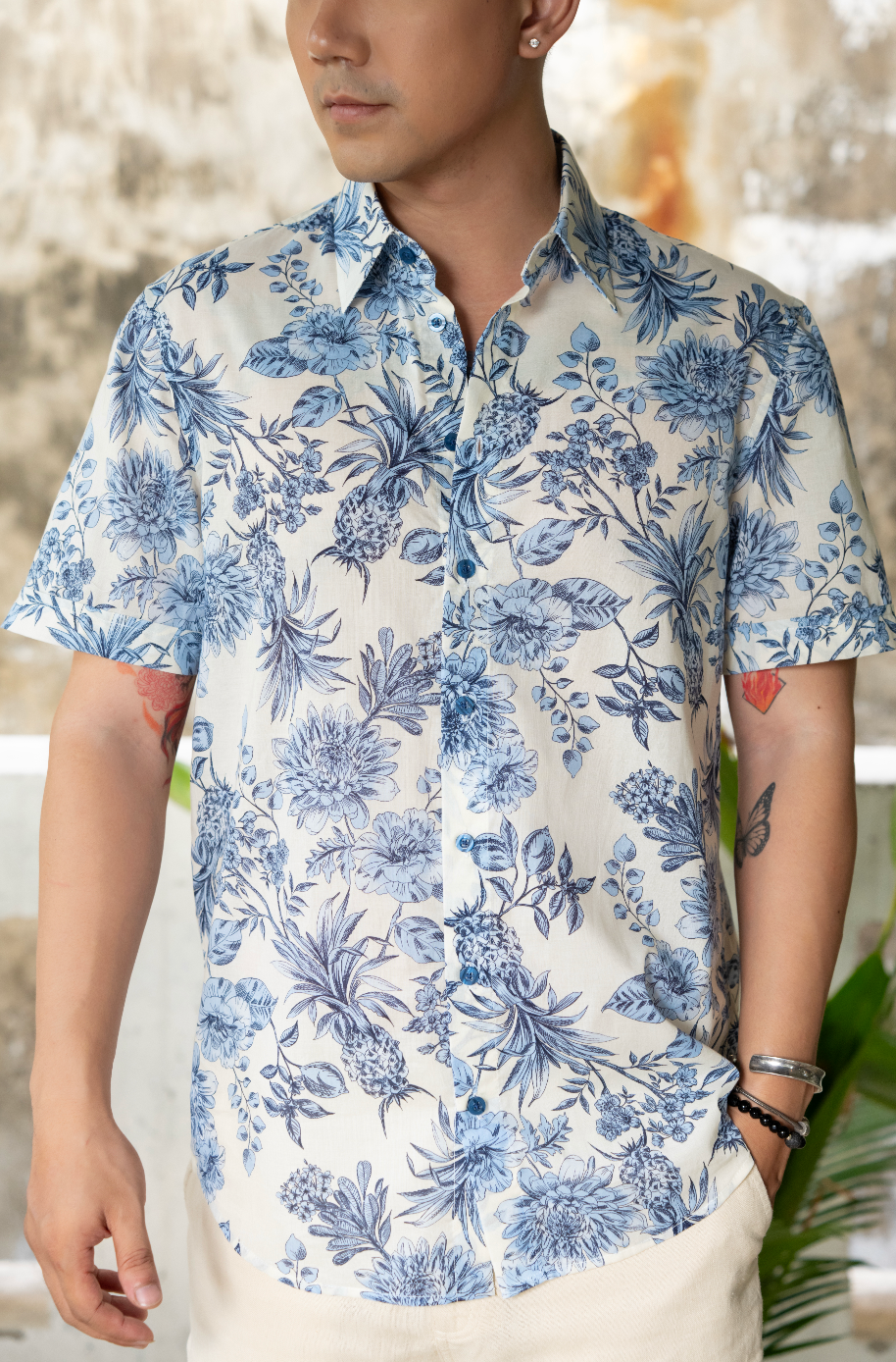 Close up shot of man wearing a blue and white floral shirt and white shorts against a textured wall.