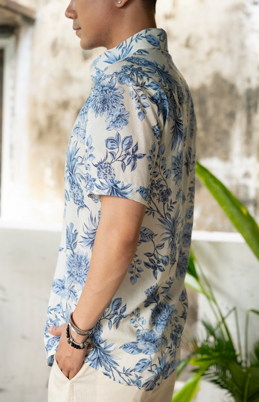 close up of side of man wearing a blue and white floral shirt and white shorts against a textured wall.