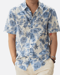 Man wearing a blue and white floral shirt and white shorts against a textured wall.