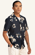 Man wearing a dark floral Hawaiian shirt and white pants on a plain background