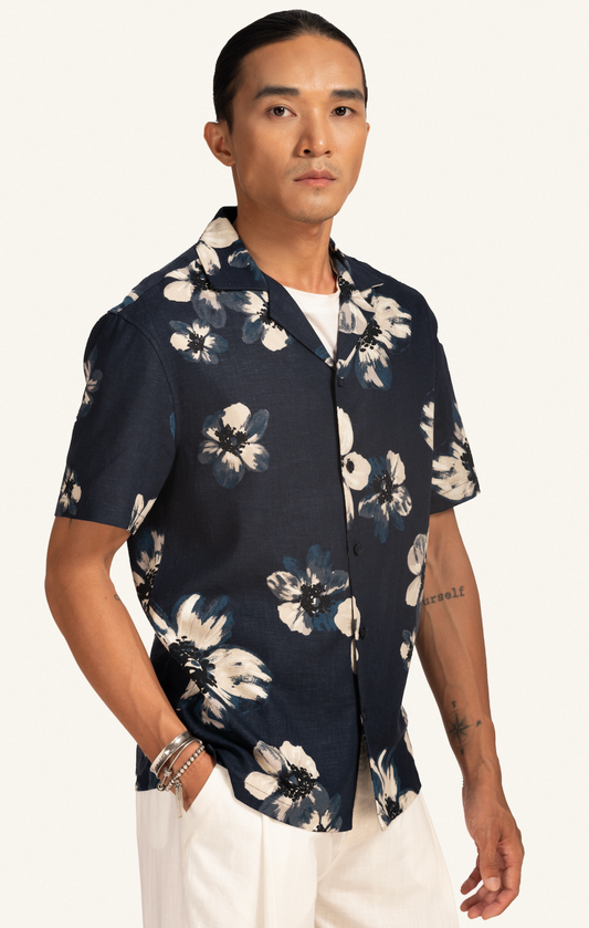 Man wearing a dark floral Hawaiian shirt and white pants on a plain background