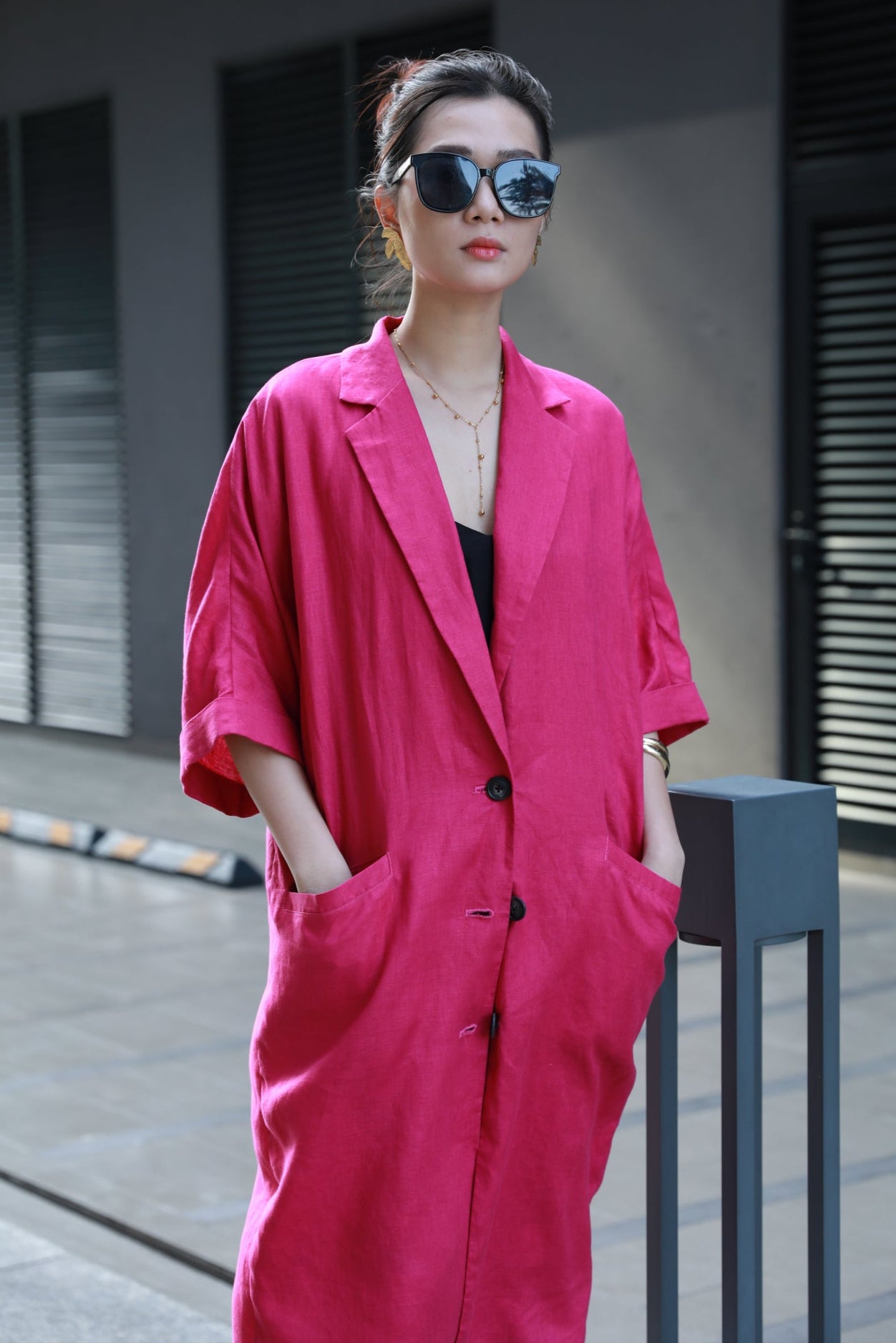 Person wearing a fuchsia pink coat with sunglasses on the sidewalk