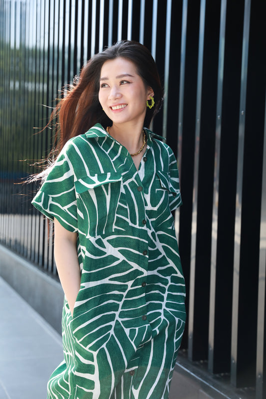 Woman wearing a green and white patterned outfit standing against a black metal fence.