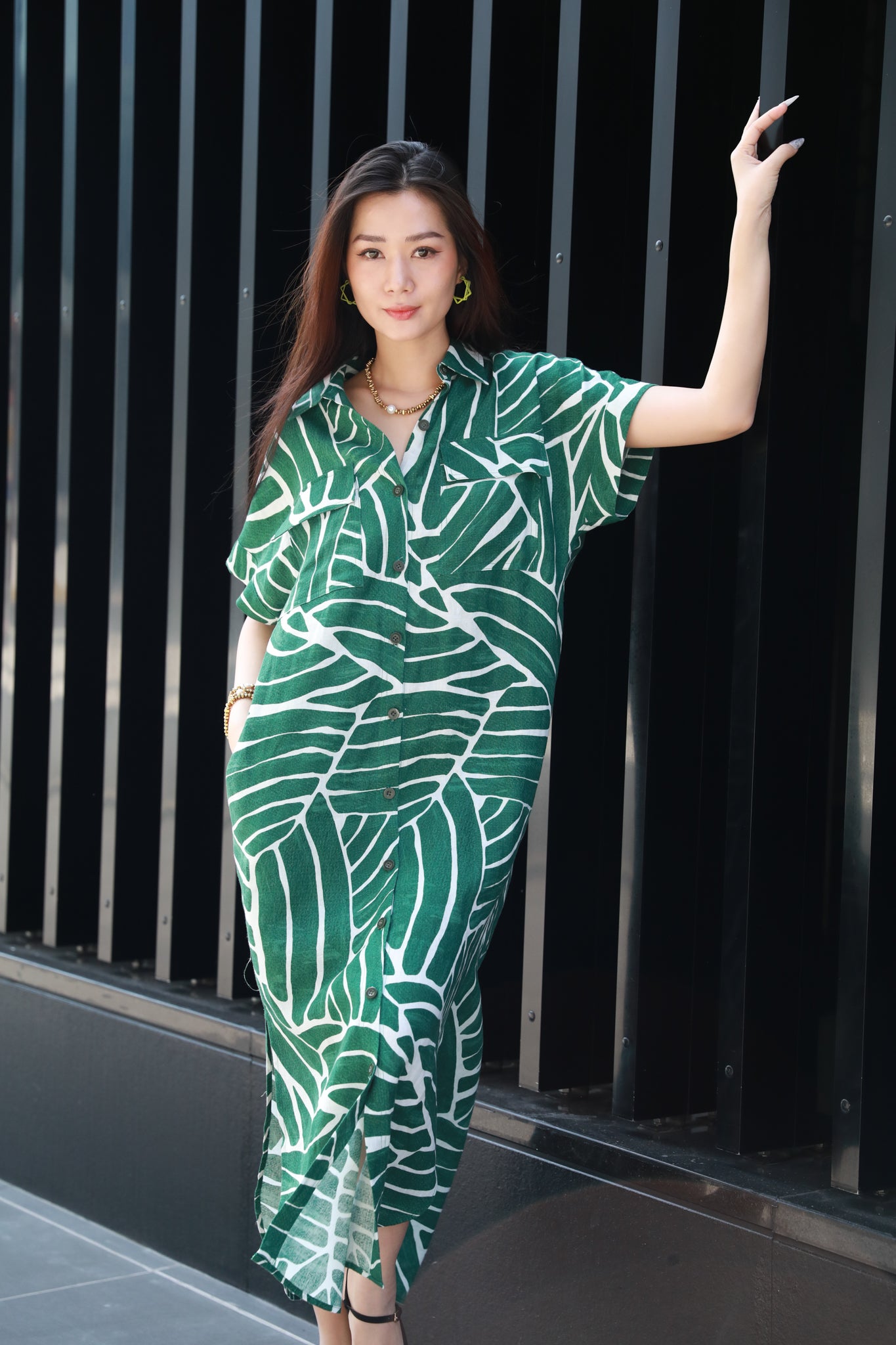 Woman in a green leaf-patterned dress posing against a black metal gate.