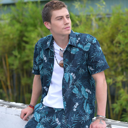 Man wearing a floral tropical shirt sitting outdoors with greenery in the background