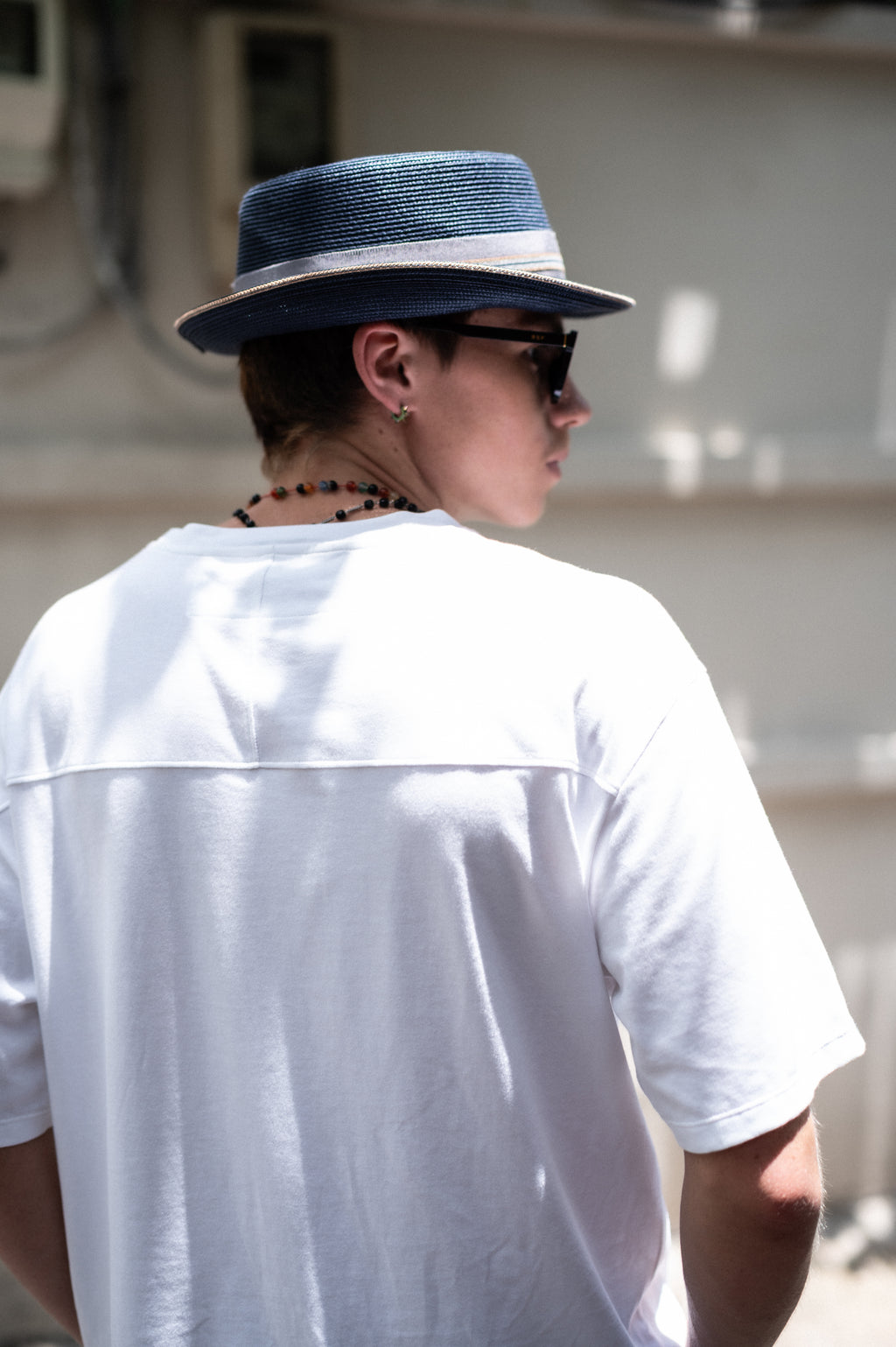 Person wearing a blue hat and sunglasses,  white t-shirt showing back yolk detail. facing away from the camera.