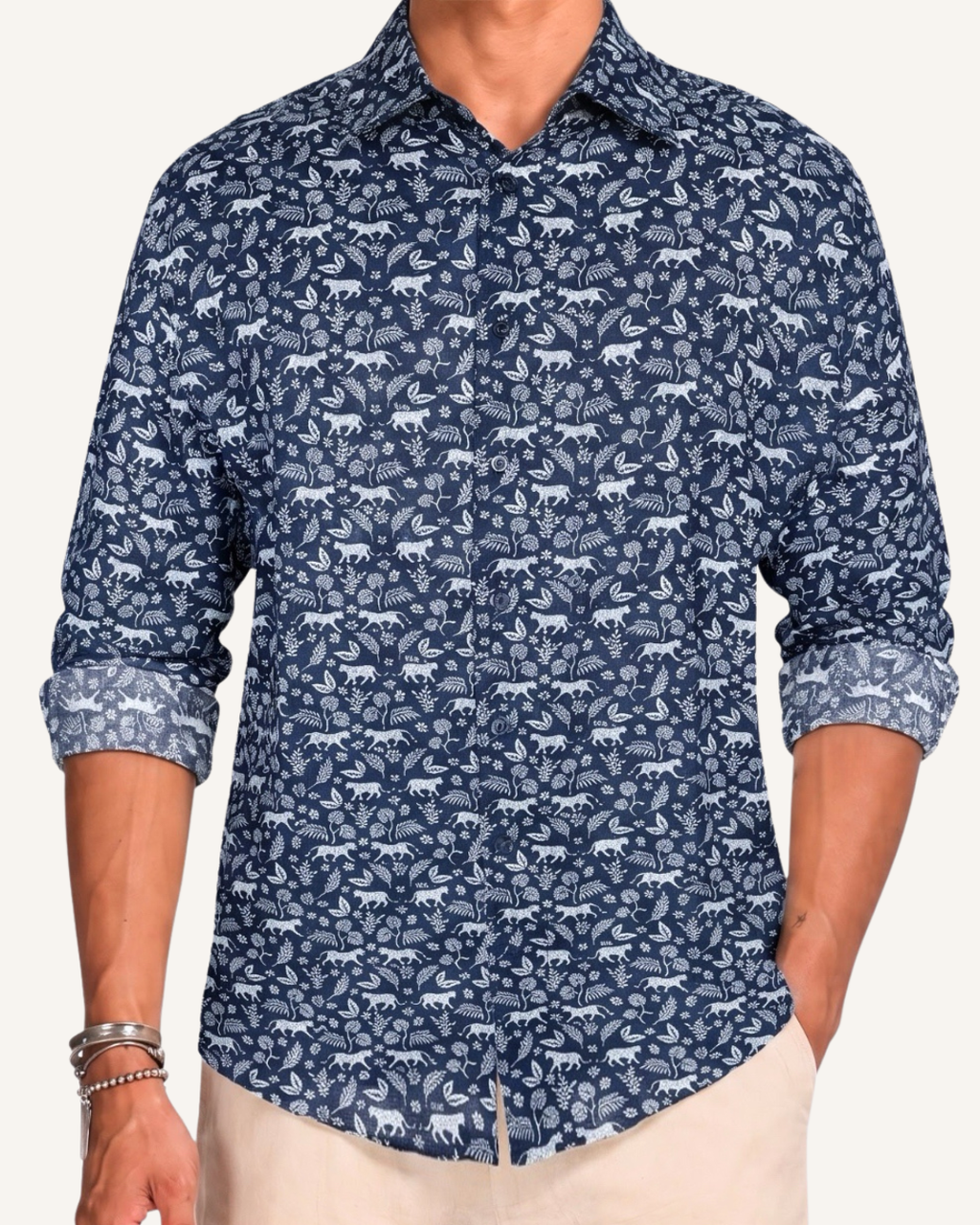 Man wearing a navy long-sleeve button-up shirt with an allover white leopard and floral print, sleeves rolled to the forearm, paired with cream trousers