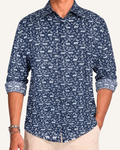 Man wearing a navy long-sleeve button-up shirt with an allover white leopard and floral print, sleeves rolled to the forearm, paired with cream trousers