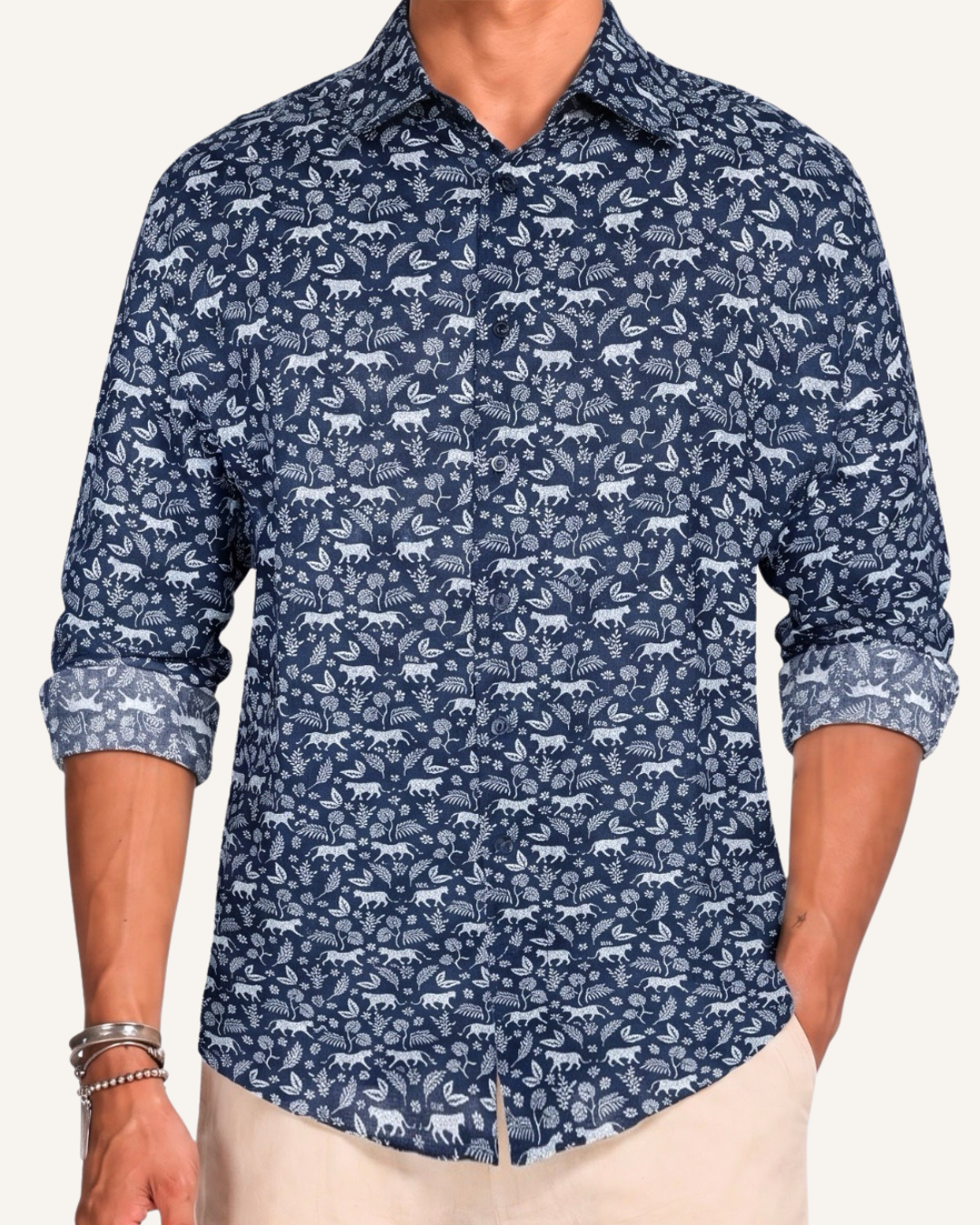 Man wearing a navy long-sleeve button-up shirt with an allover white leopard and floral print, sleeves rolled to the forearm, paired with cream trousers