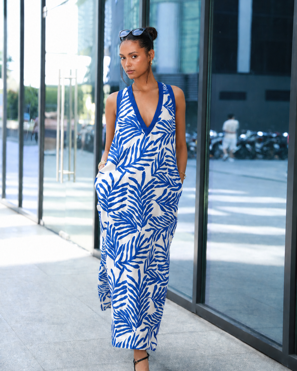 Woman wearing a blue and white floral maxi dress, walking outdoors near a glass building