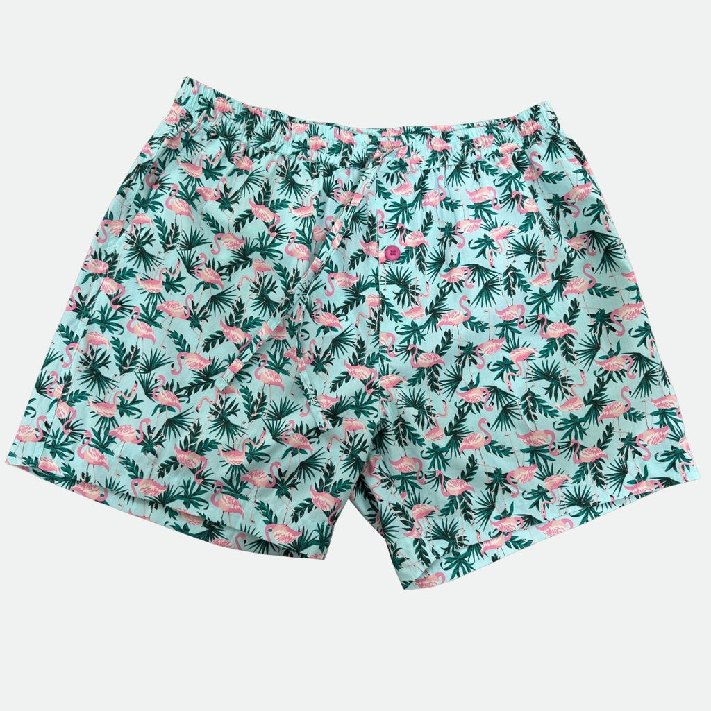 Pink Flamingo and green tropical leaf patterned lounges shorts on a light gray background - lay flat front view