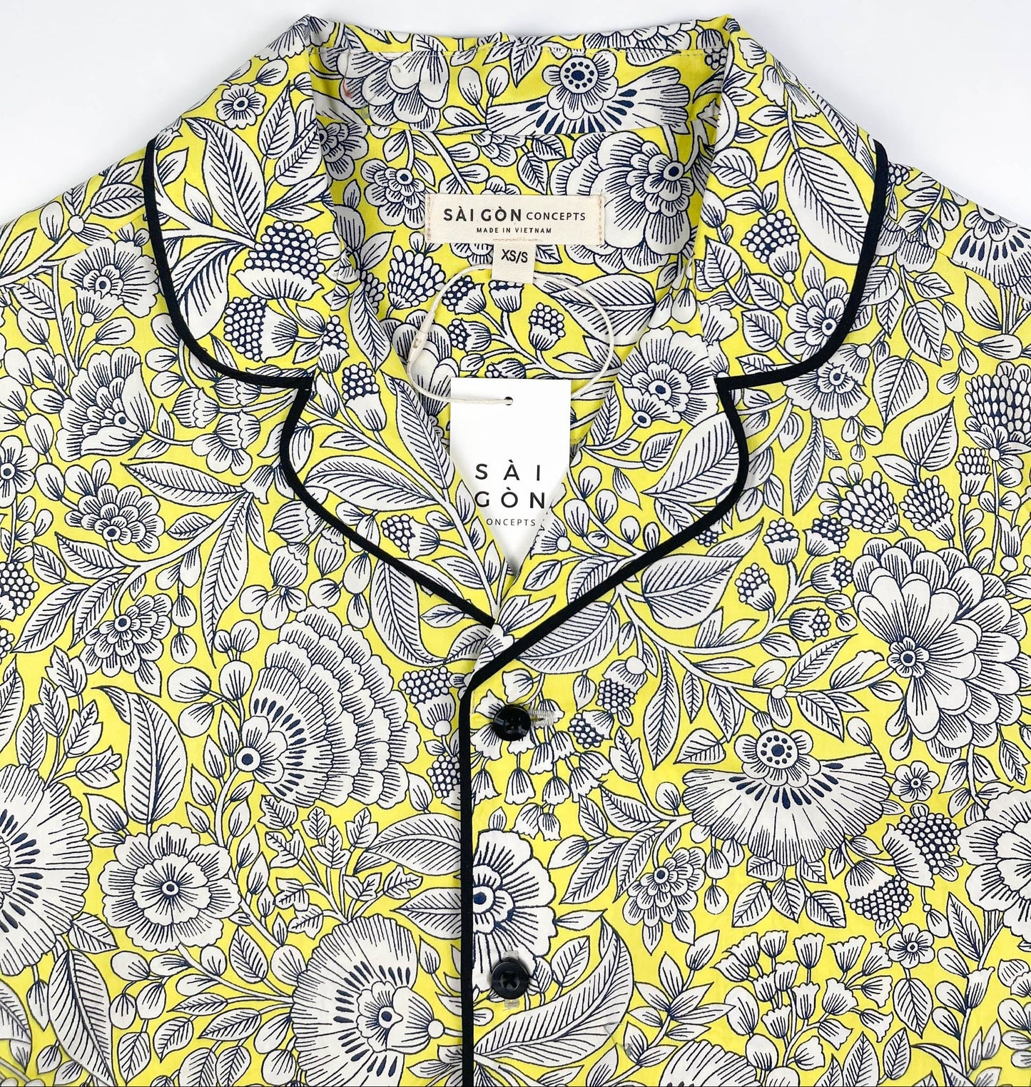 Sunshine Chintz short sleeve pyjama top lay flat close up of collar, yellow cotton with grey floral print with black contrast piping. Saigon Concepts