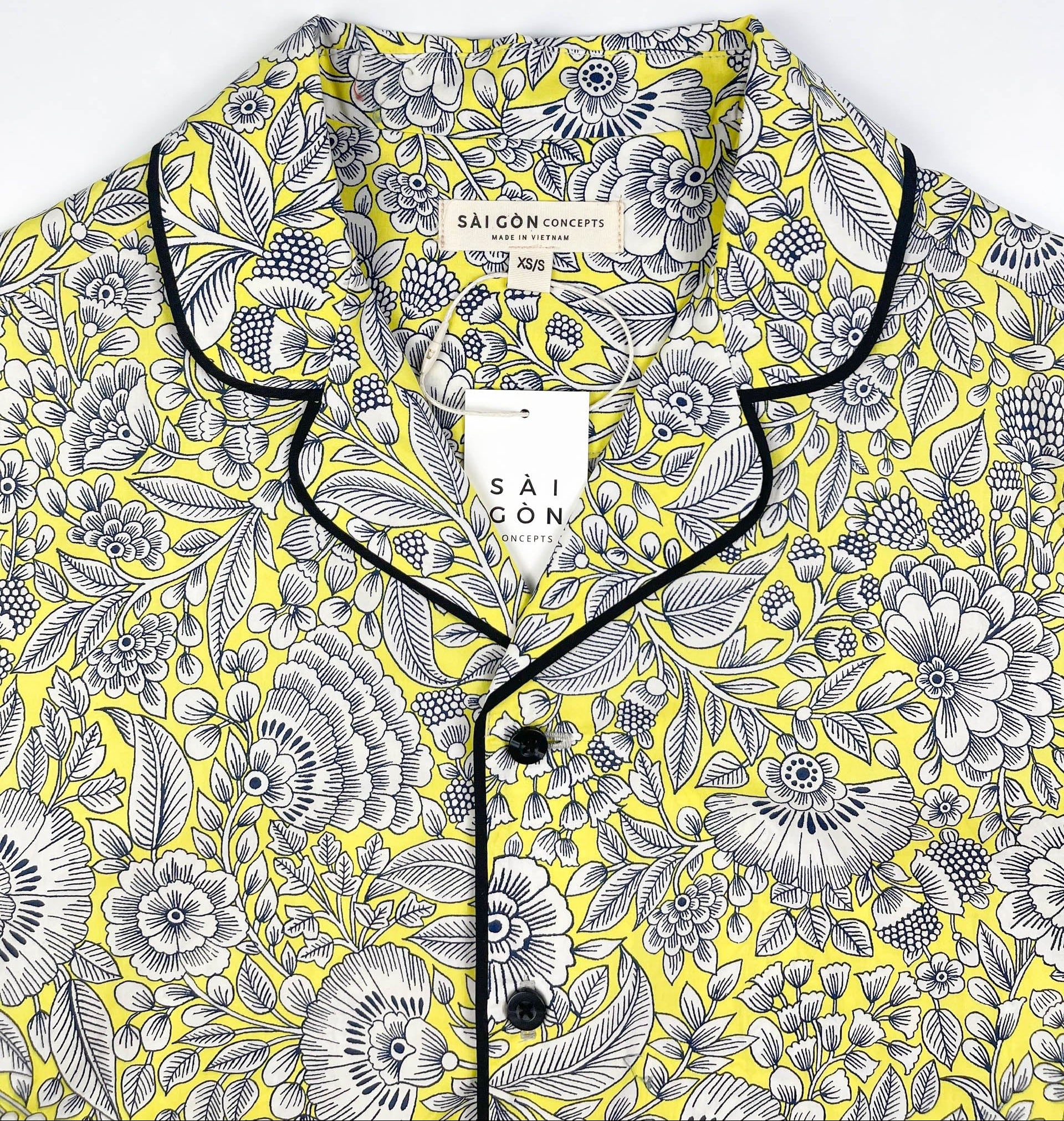 Sunshine Chintz short sleeve pyjama top lay flat close up of collar, yellow cotton with grey floral print with black contrast piping. Saigon Concepts