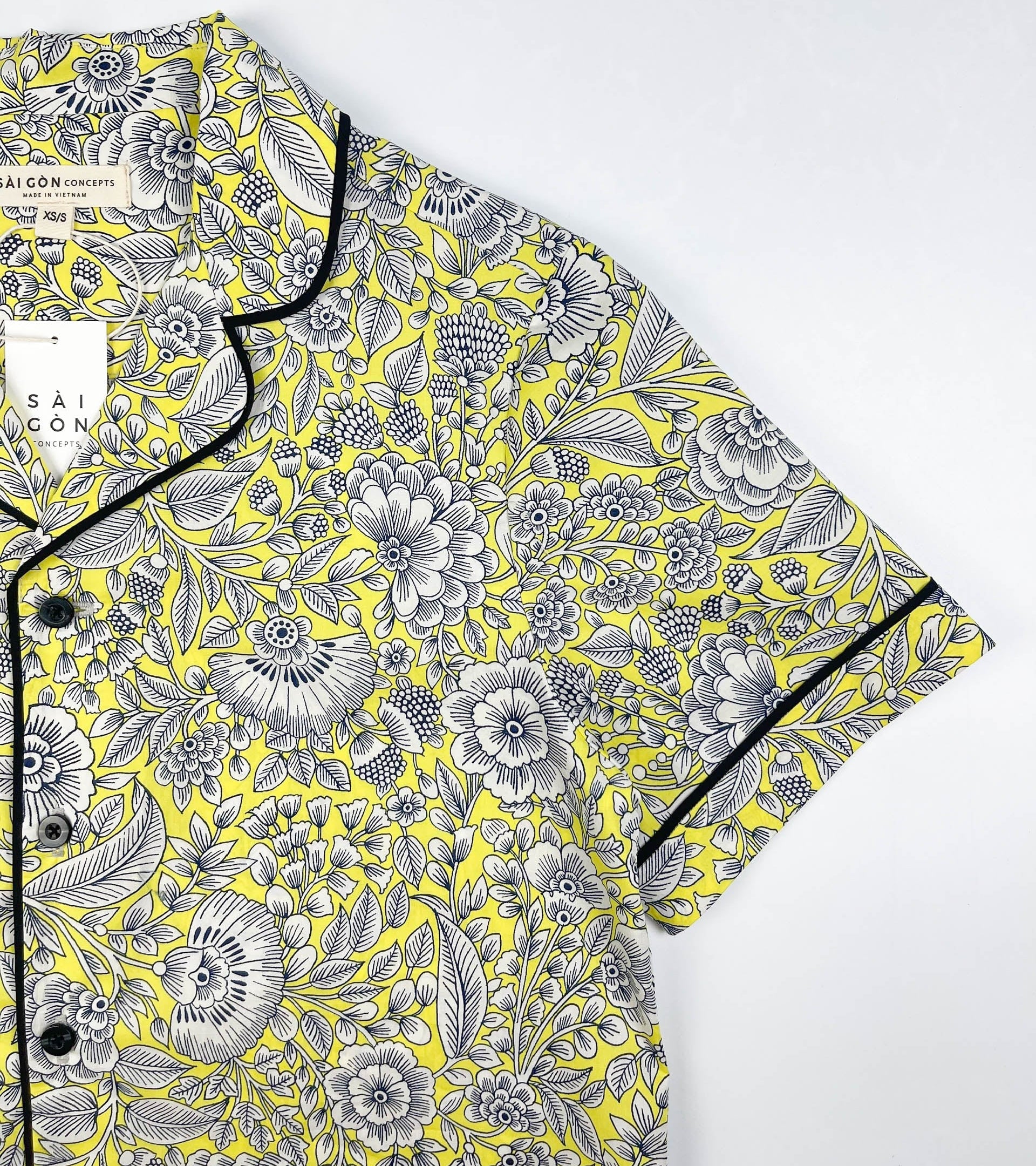 Sunshine Chintz short sleeve pyjama top lay flat image of sleeve detail, yellow cotton with grey floral print with black contrast piping on sleeves, collar and front. Saigon Concepts
