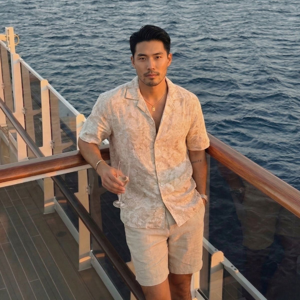 Man standing on a boat deck holding a glass of wine with ocean in the background wearing Saigon Concepts Ivory coloured Hawaiian Shirt with Ivory Hibiscus floral etching print