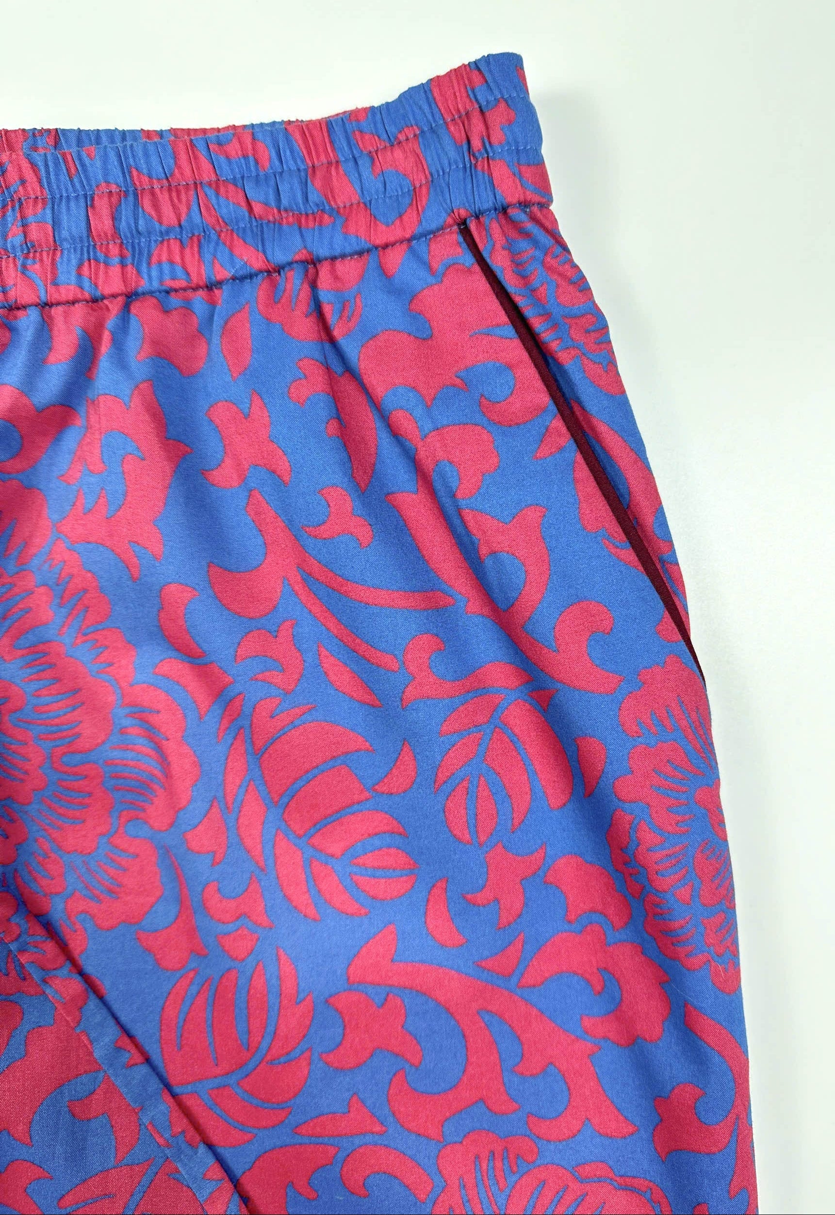 Saigon Concepts - Close-up of Jardin Royale waistband detail in cotton fabric showing vibrant red-pink and sea note blue floral print with dark wine piping trim on pocket