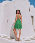 Woman wearing a green low-back camisole dress, back view outdoors against a white building