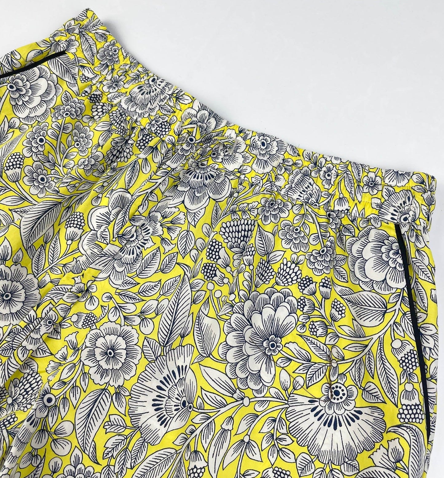 Sunshine Chintz pyjama shorts lay flat image of elasticated waistband and black contrast piping on pockets. Yellow cotton with grey floral print - Saigon Concepts