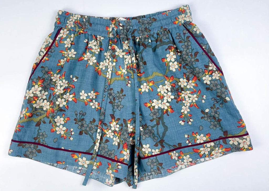 Female Lounge Shorts in teal blue with white blossom floral print. Flat front view with drawstring cord and 2 side pockets with burgundy contrast piping on seams - Saigon Concepts
