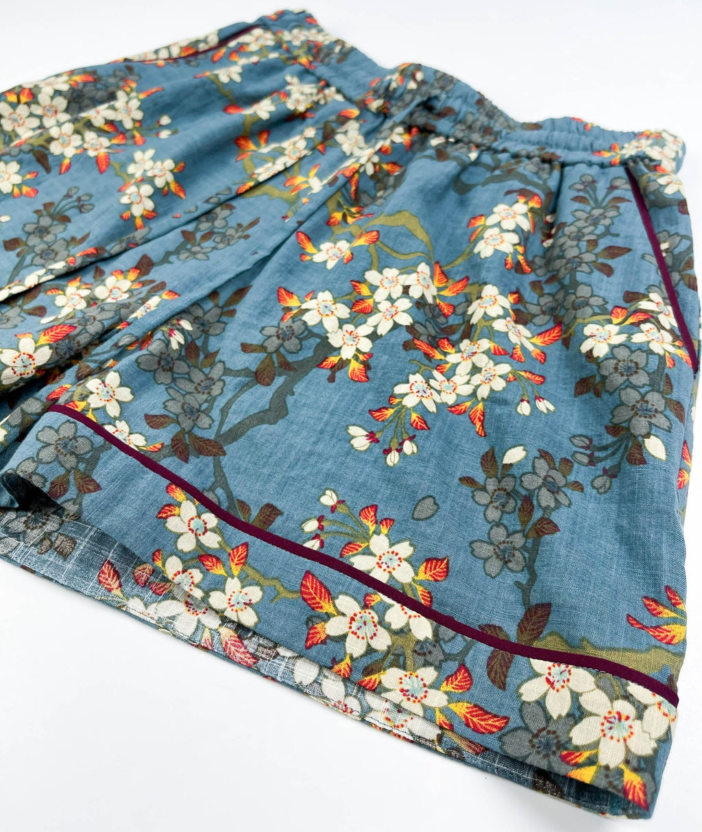 Female Lounge Shorts in teal blue with white blossom floral print. Flat front view show leg seam detail with burgundy contrast piping - Saigon Concepts