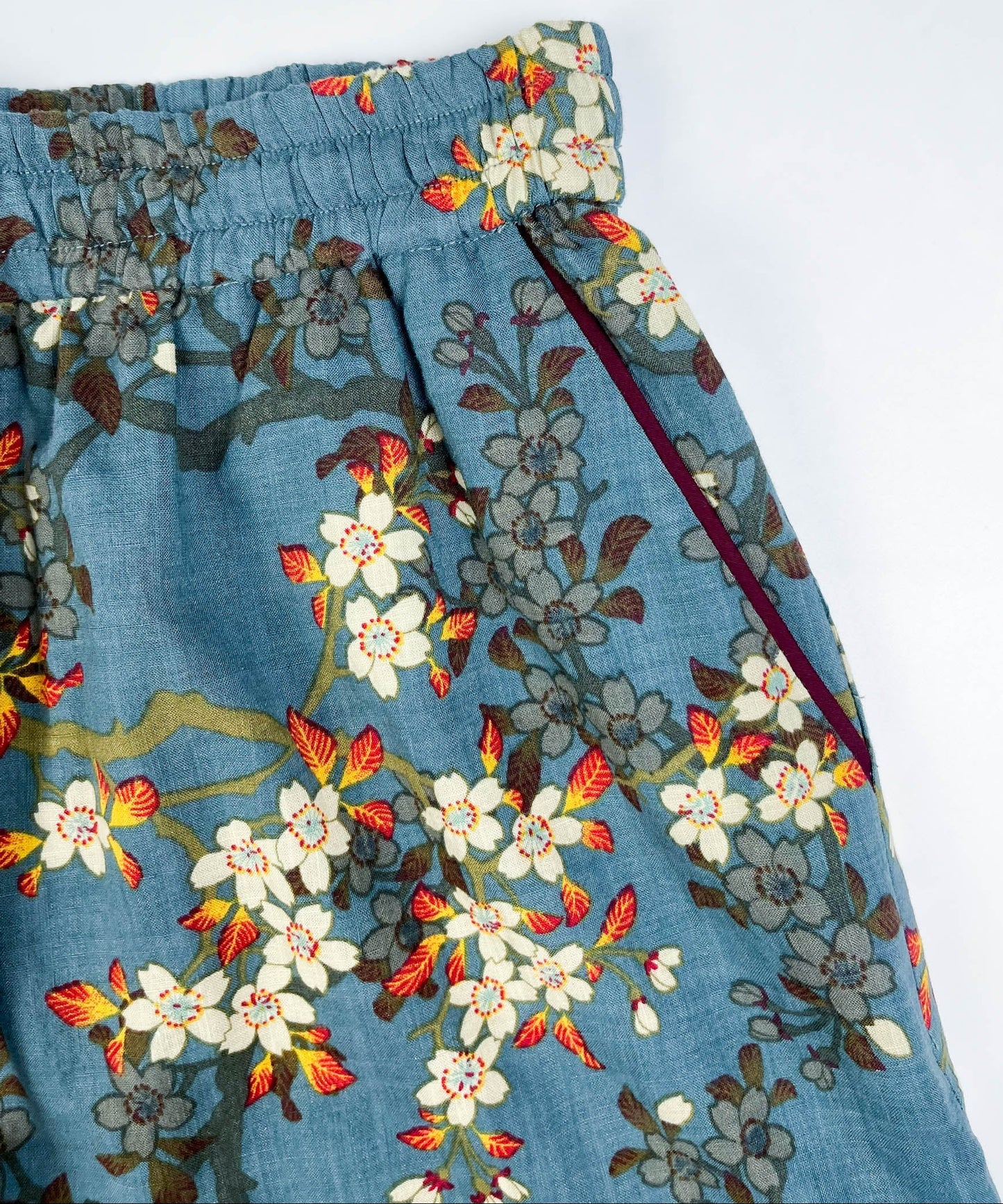 Female Lounge Shorts in teal blue with white blossom floral print. Flat front view of side pocket with burgundy contrast piping on seam - Saigon Concepts