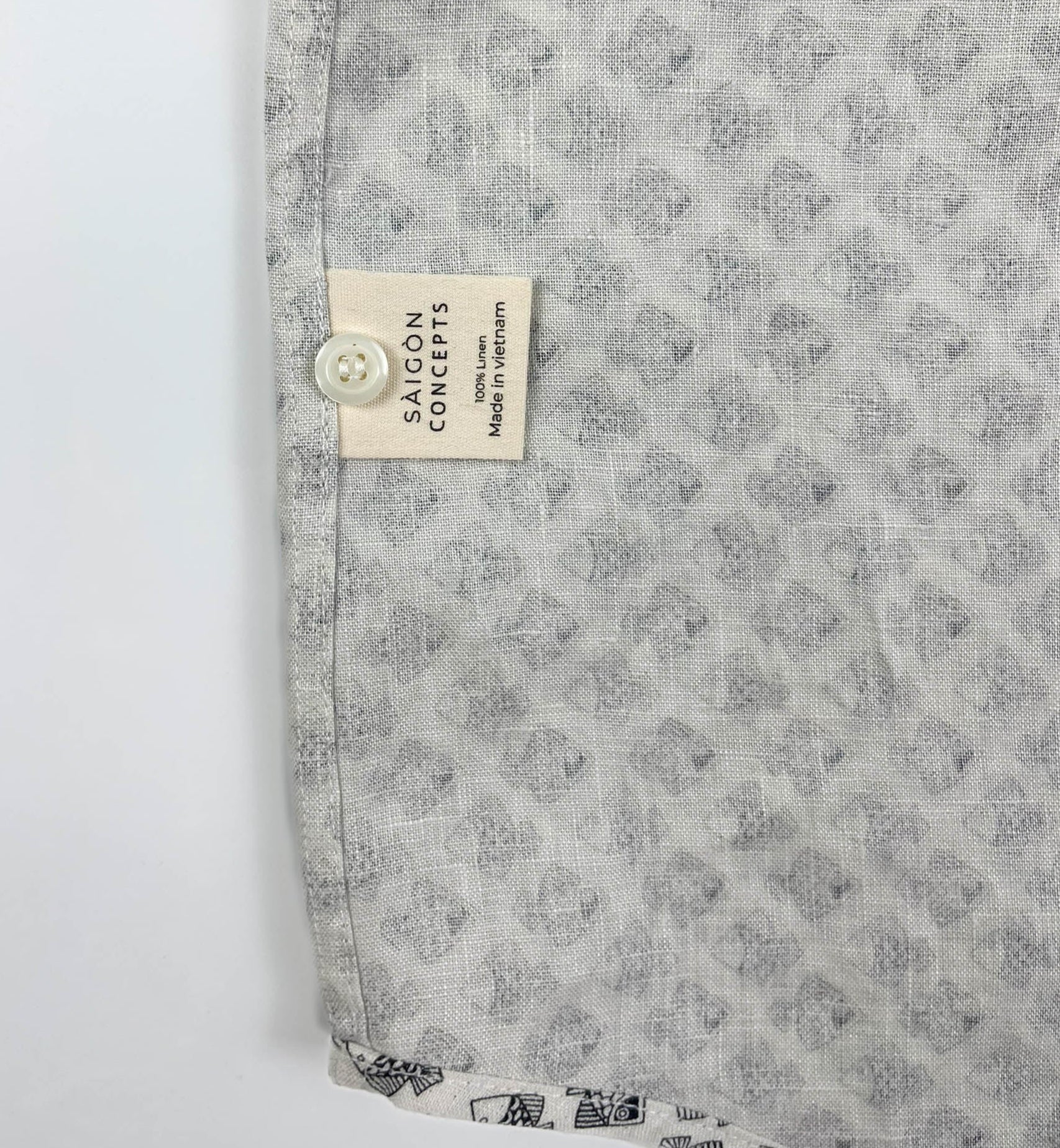 Tiny Black Fish linen long sleeve button-up shirt lay flat care label detail view, small fish print on natural white base