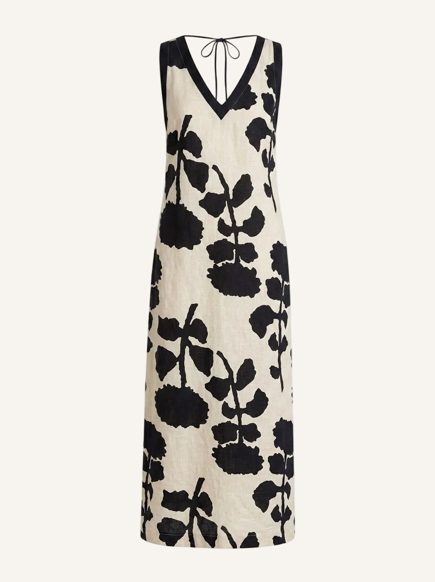 A sleeveless V-neck maxi dress with a black and cream floral print, featuring a tie-neck detail at the back, shown against a plain off-white background.