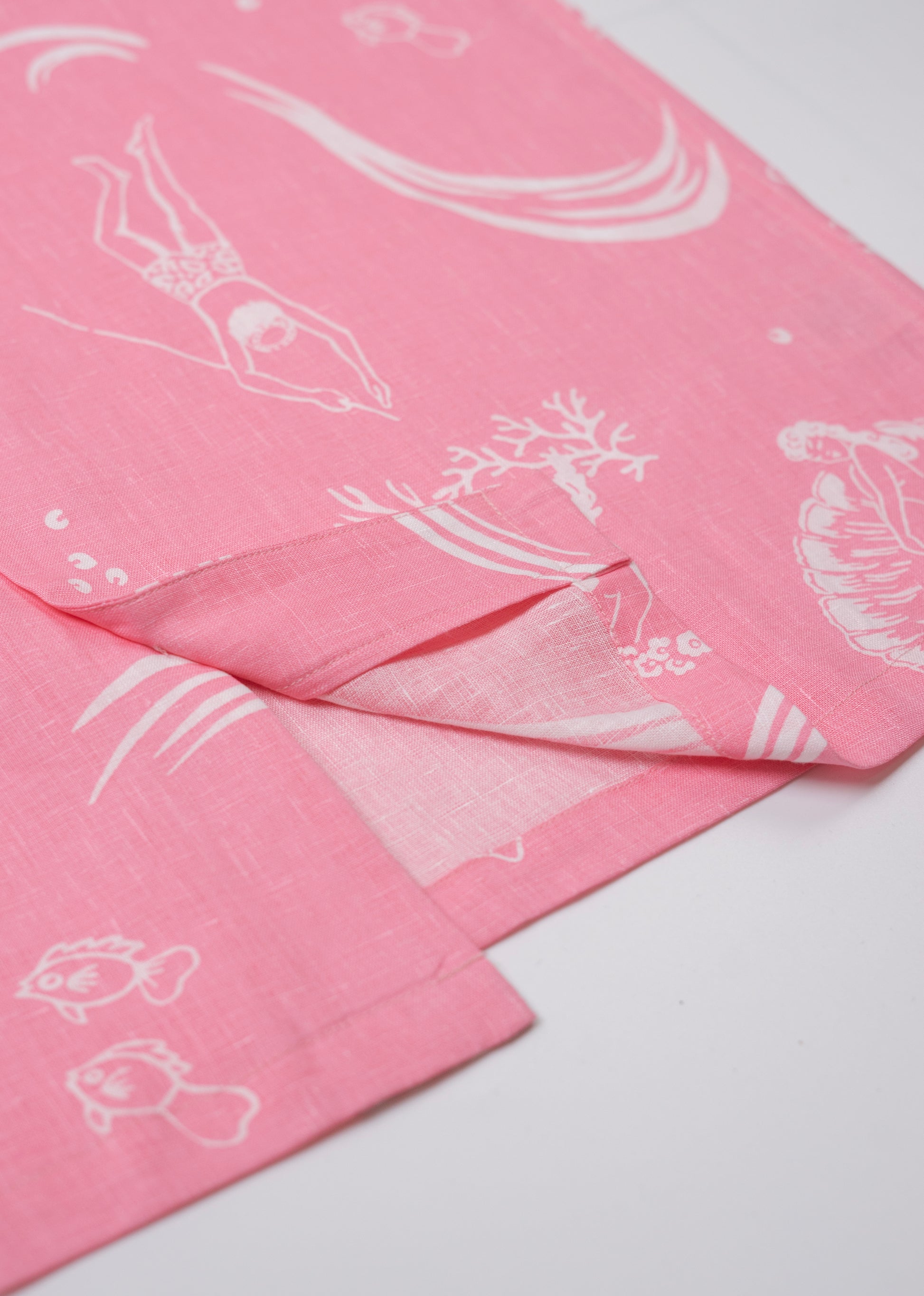 Saigon Concepts Coral Dream 100% Linen Hawaiian Shirt a pink base fabric with while drawn etchings of mermaids, fish and surfers - seam detail view