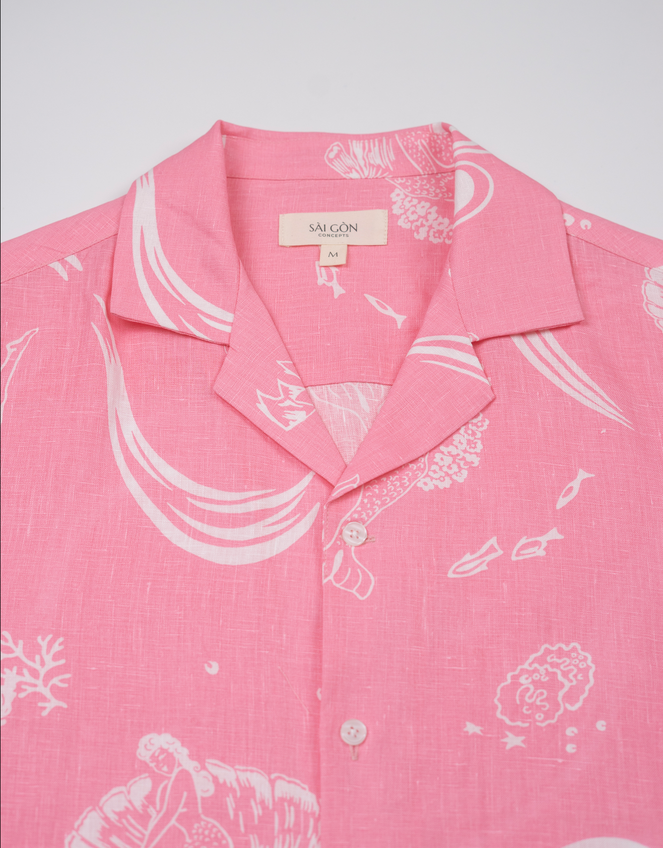 Saigon Concepts Coral Dream 100% Linen Hawaiian Shirt a pink base fabric with while drawn etchings of mermaids, fish and surfers - neck detail view