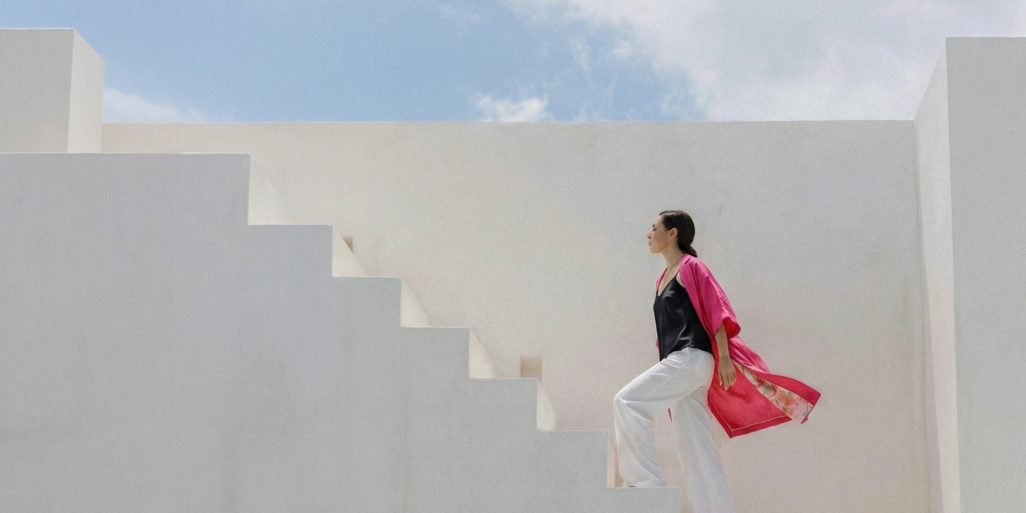 Woman standing on a white architectural structure with a pink funchsia coat, blue sky in the background